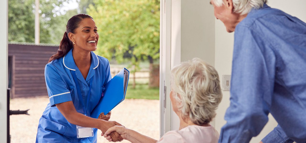 Home-health-aide-greeting-senior-couple-at-their-home